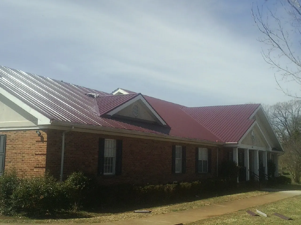 Red metal roof with gabled entries on a long brick building, from a Hail Damage Roof Repair job in Highland Park